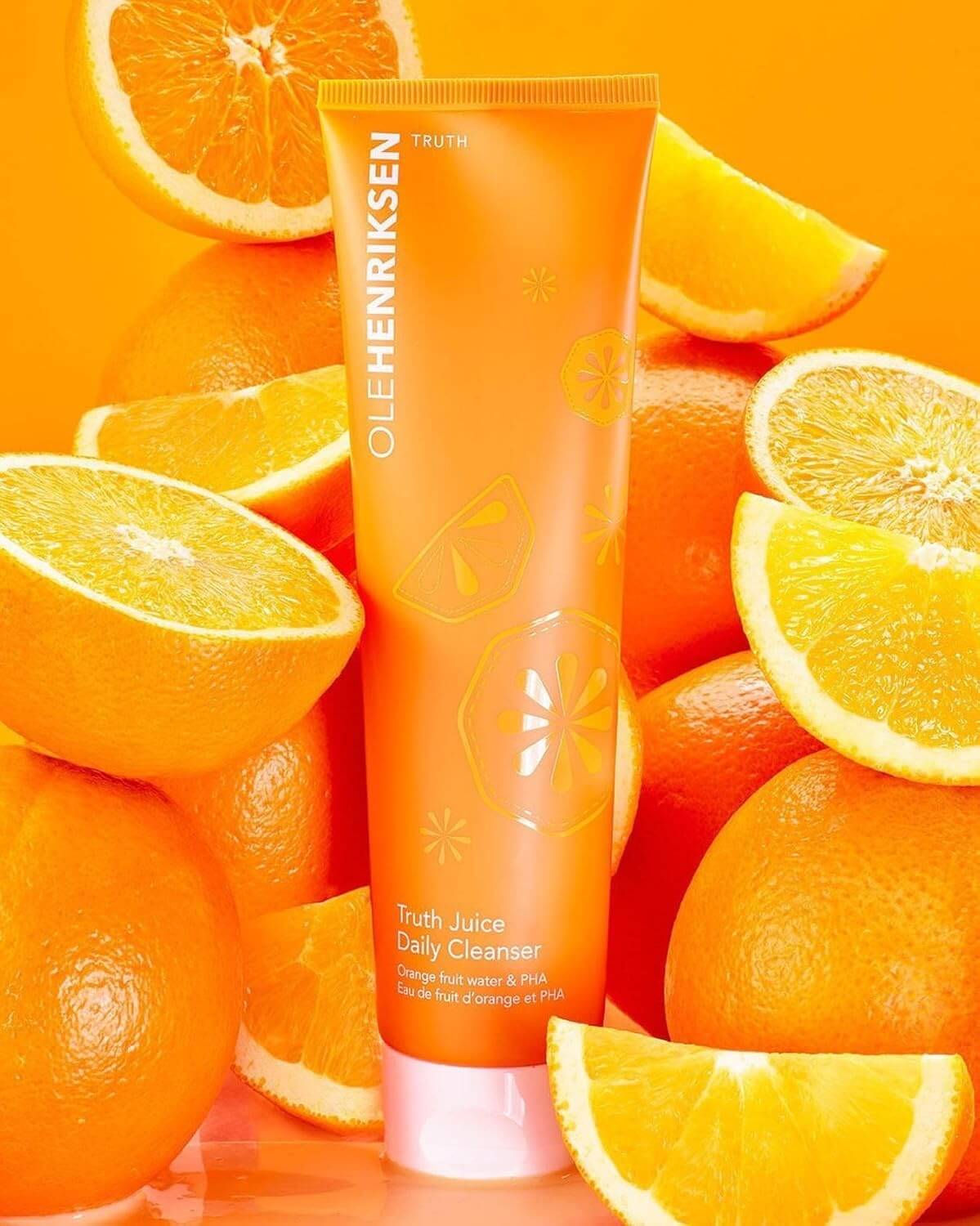 Tube of Ole Henriksen Truth Juice Daily Cleanser surrounded by sliced oranges on an orange background