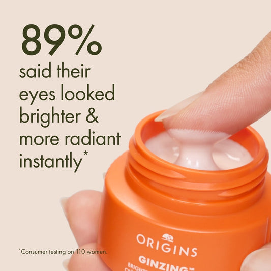 Orange jar of Origins eye cream with a hand holding it, on a beige background.