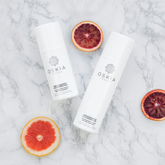 Two Oskia skincare products on a marble surface with sliced blood oranges.