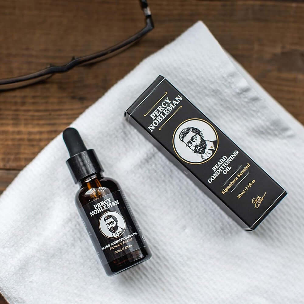 Bottle and box of Percy Nobleman product on a white towel with glasses and camera in the background.