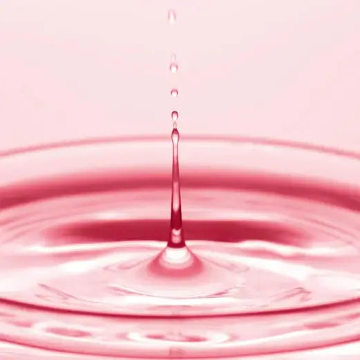 Close-up of water droplets falling into a pink-hued liquid surface, creating ripples.