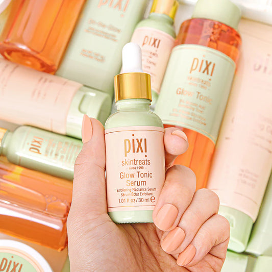 Hand holding a PIXI skincare serum bottle with other PIXI products in the background