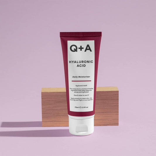 Tube of Q+A Hyaluronic Acid Moisturizer on a wooden block with a purple background