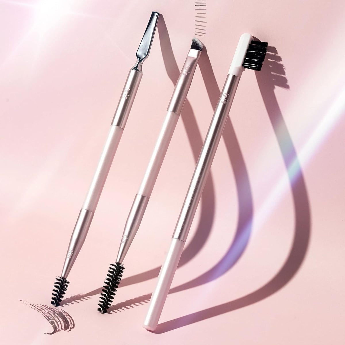 Real Techniques Three makeup brushes with black bristles on a pink background