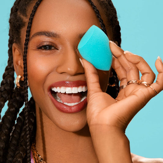 Woman using a blue makeup sponge on her face against a blue background