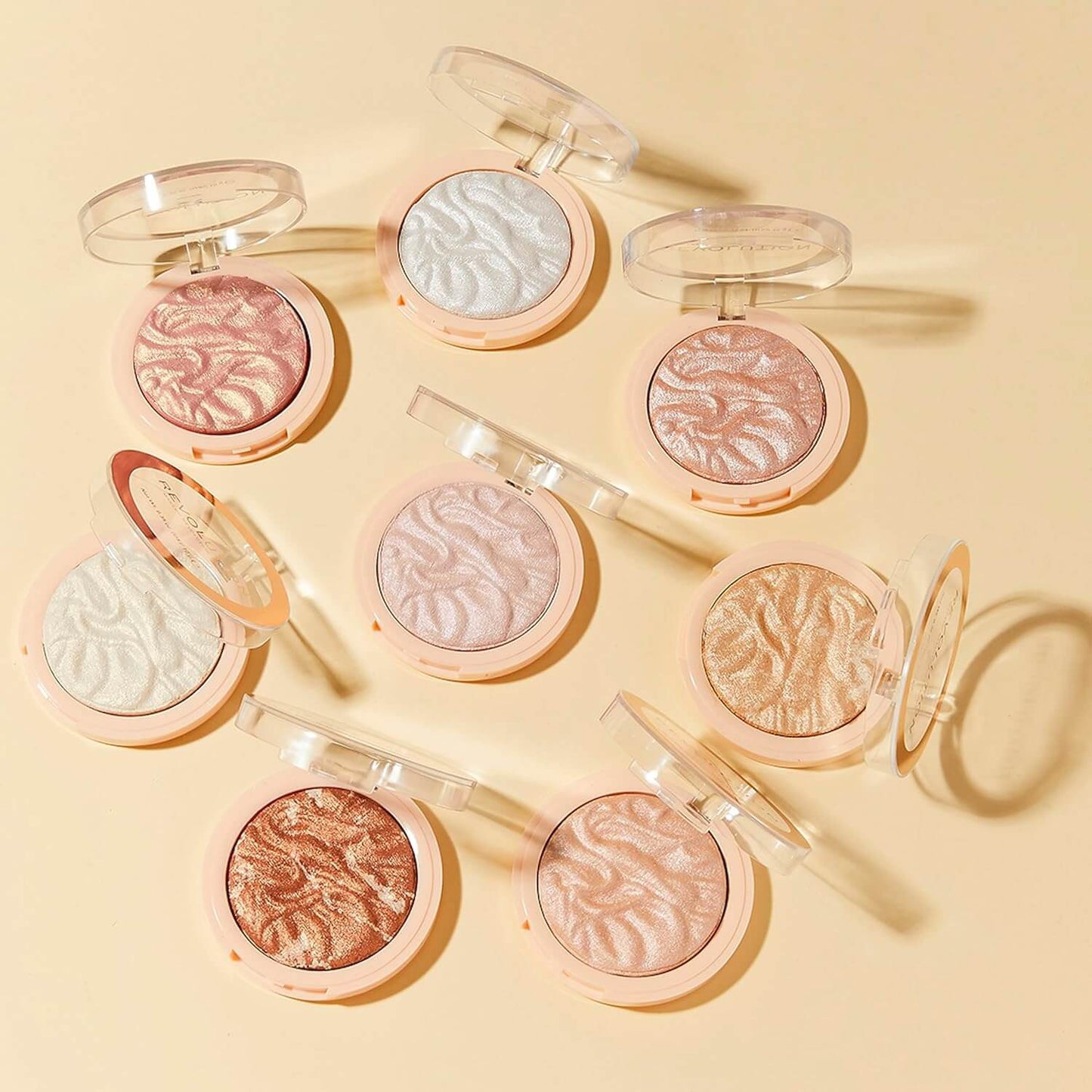 Multiple Revolution compact makeup powders with various shades on a beige background