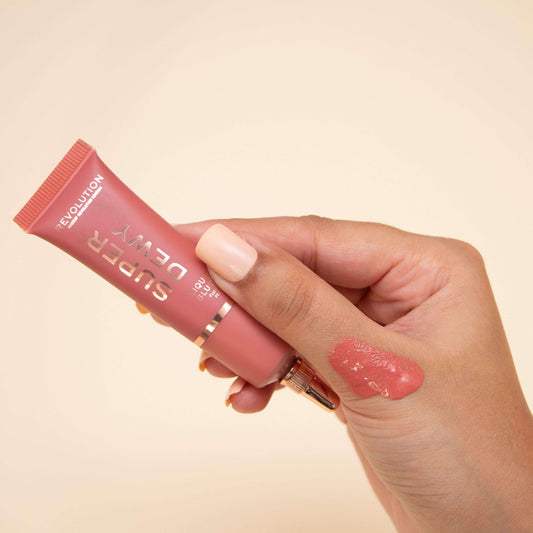Close-up of a hand holding Revolution Superdewy Liquid Blush tube with a swatch on the skin, showcasing its color.