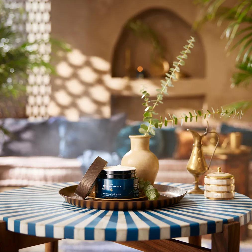 RITUALS The Ritual of Hammam Body Cream on a stylish table, surrounded by decorative elements and plants, evoking a serene setting.