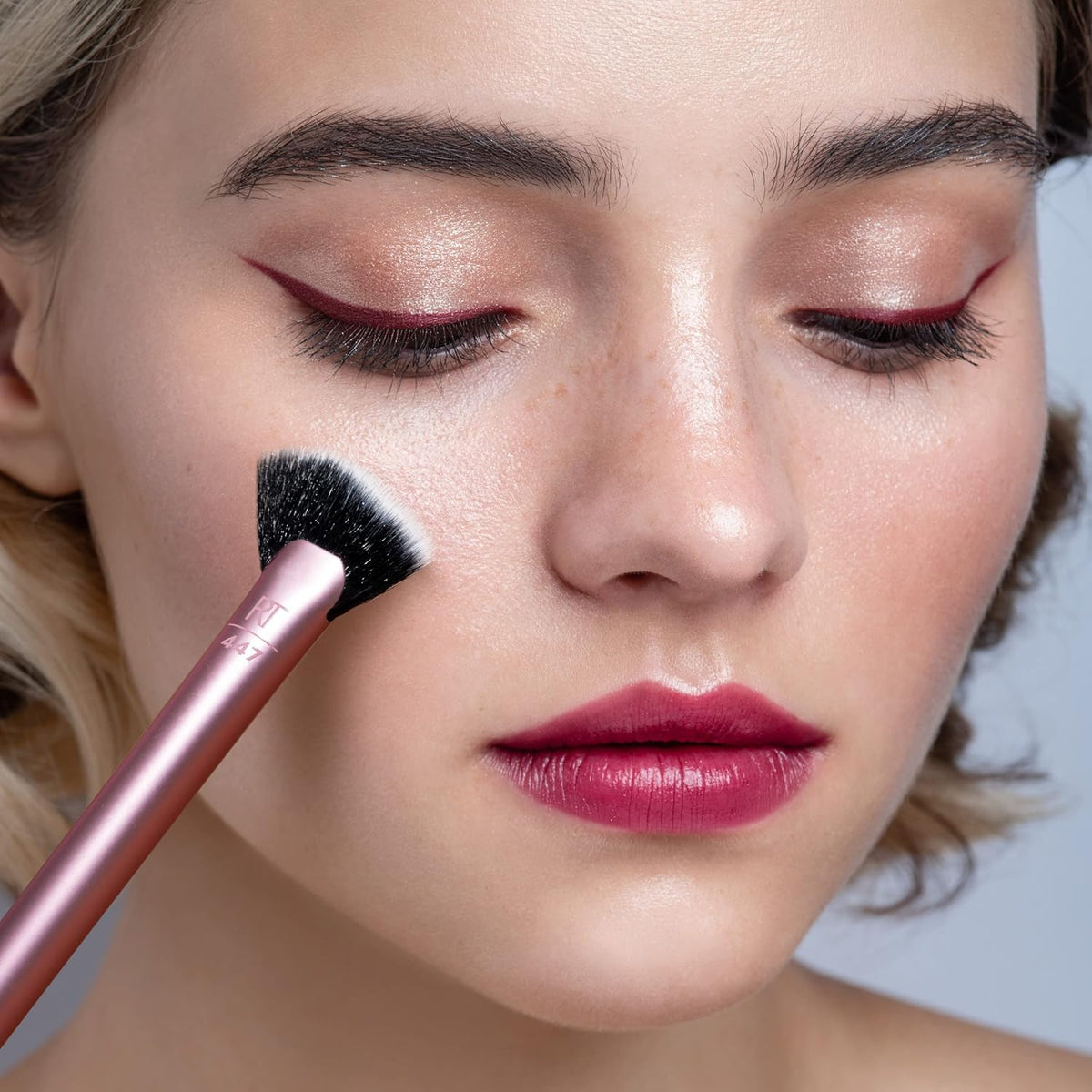 Close-up of a woman applying makeup with a brush on her face.