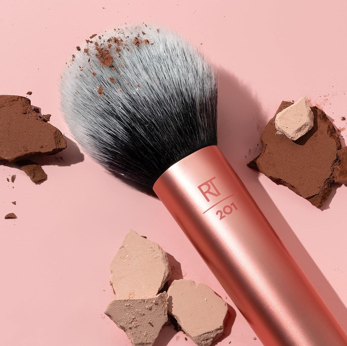 Makeup brush with rose gold handle and 'RV' logo on a pink background with makeup powder.