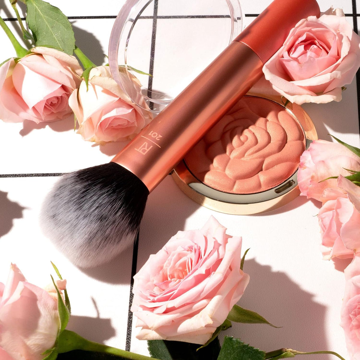 Makeup brush and compact with pink roses on a white surface