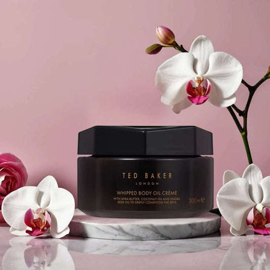 Black jar of Ted Baker Whipped Body Oil Creme with white orchids on a pink background