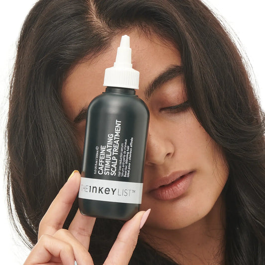 The INKEY List Caffeine Stimulating Scalp Treatment bottle held by a model showcasing its benefits for hair health.