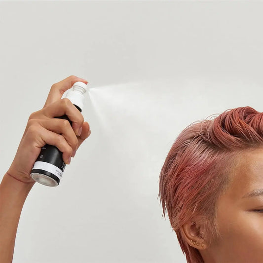 Person using The INKEY List PCA Bond Repair Hair Treatment spray on styled hair for revitalization.