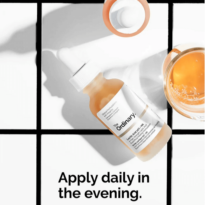 The Ordinary Lactic Acid 10% + HA 2% serum bottle on a tiled surface with text 'Apply daily in the evening'.