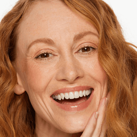 Close-up of a smiling woman with wavy red hair, showcasing glowing skin and a radiant look.