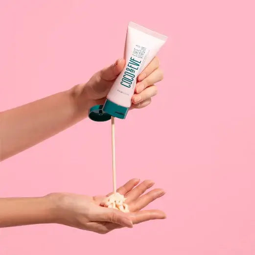 Coco & Eve Like a Virgin Coconut & Fig Hair Mask being poured onto a hand against a pink background.