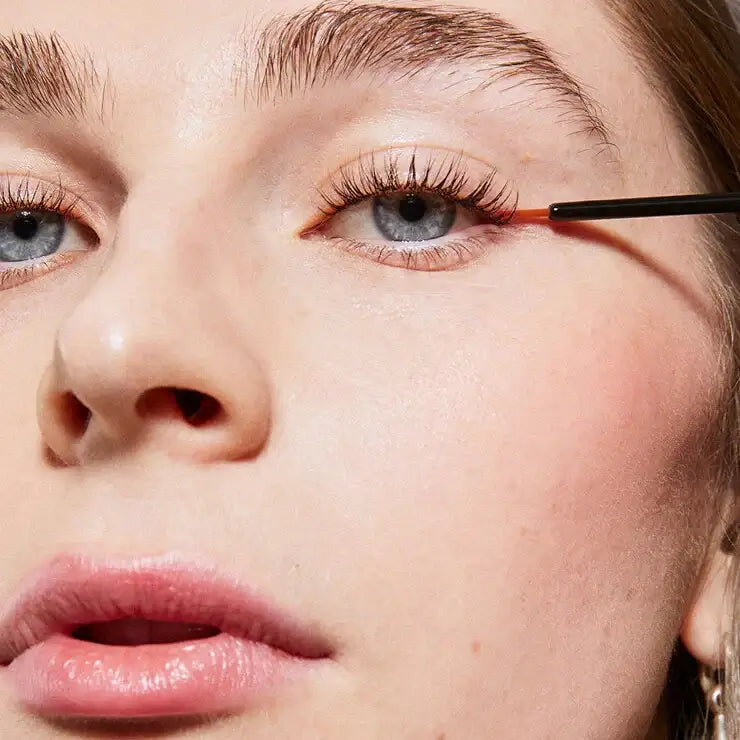 Close-up of a person applying XLash eyeliner with a brush.