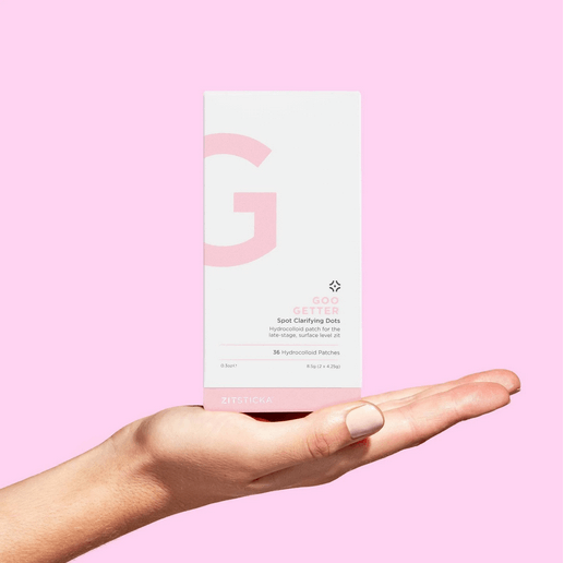 Hand holding a ZITSTICKA skincare product box with a pink background