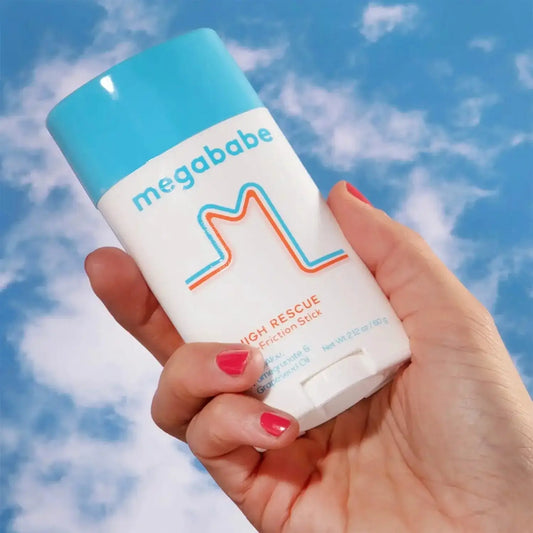 Megababe Thigh Rescue 60g friction stick held in hand against a blue sky, ideal for preventing chafing during summer.