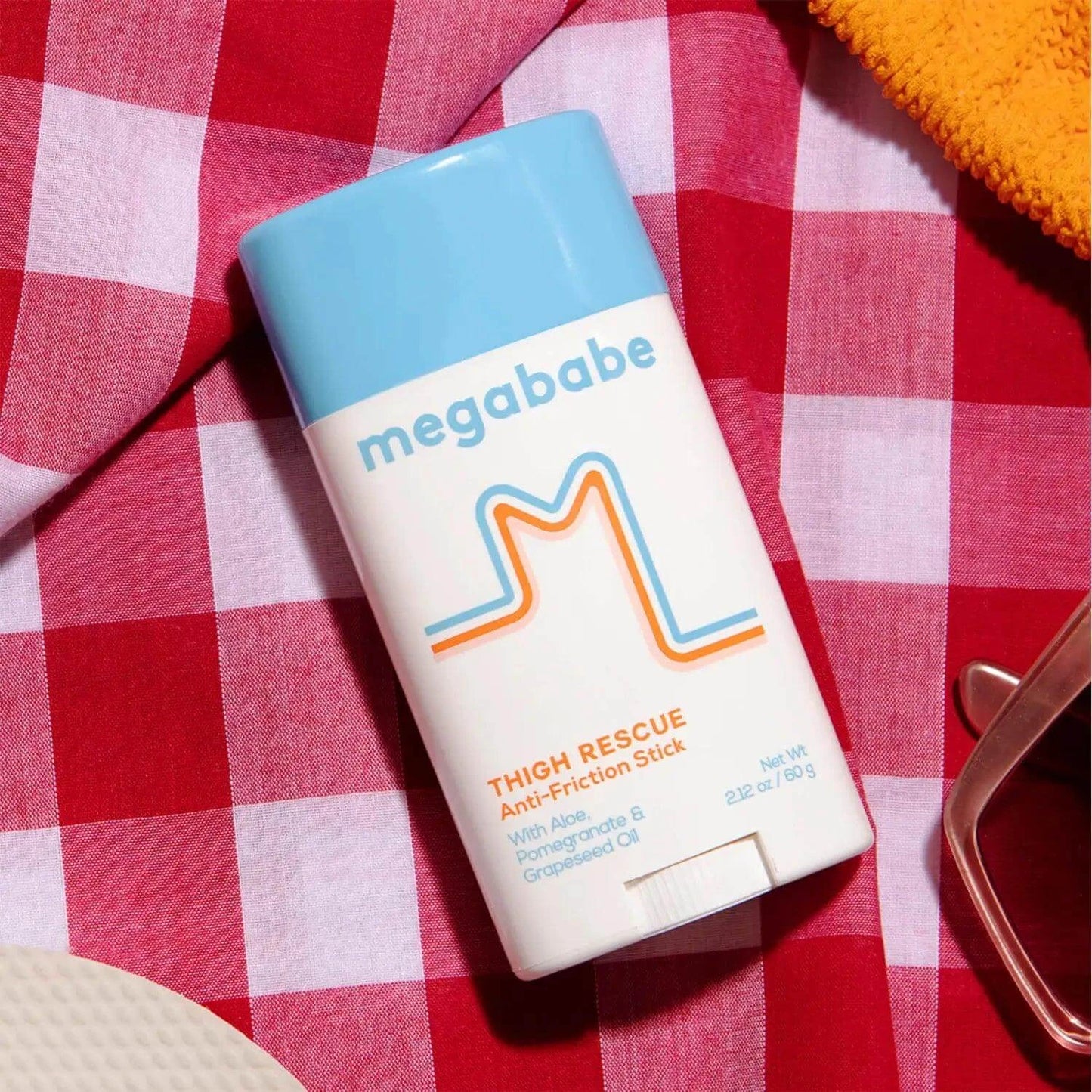 Megababe Thigh Rescue anti-friction stick on a red checkered background, designed to prevent chafing and enhance comfort.