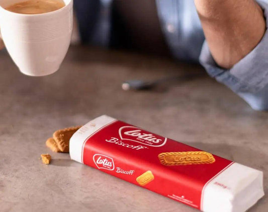 Person enjoying coffee with Lotus Biscoff Caramelised Biscuits, showcasing the iconic packaging and crunchy texture.