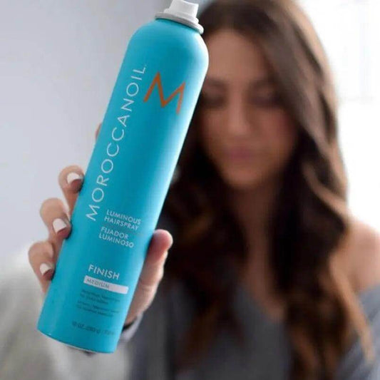 Moroccanoil Luminous Hairspray Medium 330ml spray can held by a person with soft, wavy hair, promoting flexible hold and shine.