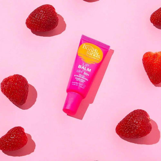 Bondi Sands SPF50+ Lip Balm 10g surrounded by fresh strawberries on a pink background, perfect for sun protection and hydration.