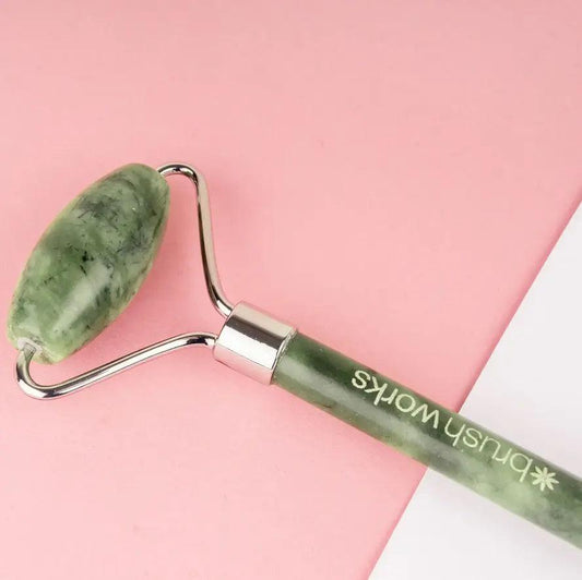Brushworks HD Jade Roller on a pink background, perfect for skin massage and reducing puffiness.
