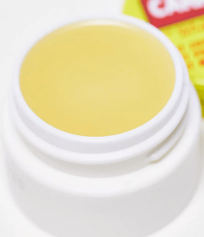 Close-up of Carmex Cherry Pot Lip Balm, yellow balm in white container, moisturizing, SPF 15 protection for dry lips.