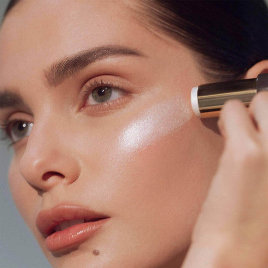 Woman applying RÓEN RÓGLOW Skin Stick highlighter for a radiant, luminous complexion.