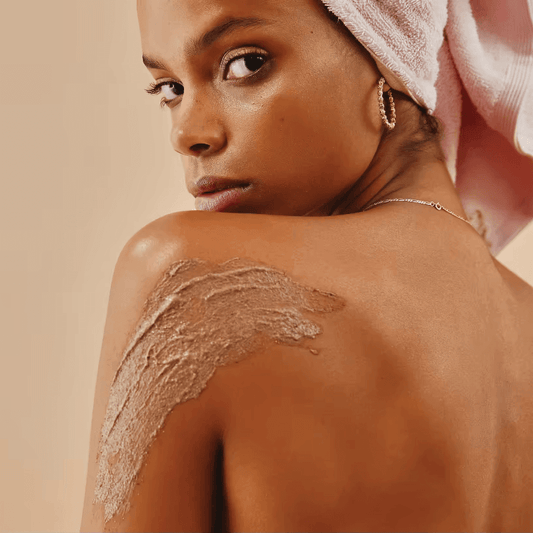 Model applying Frank Body Express-o Coffee Scrub on shoulder, with towel on head, showing skincare routine.