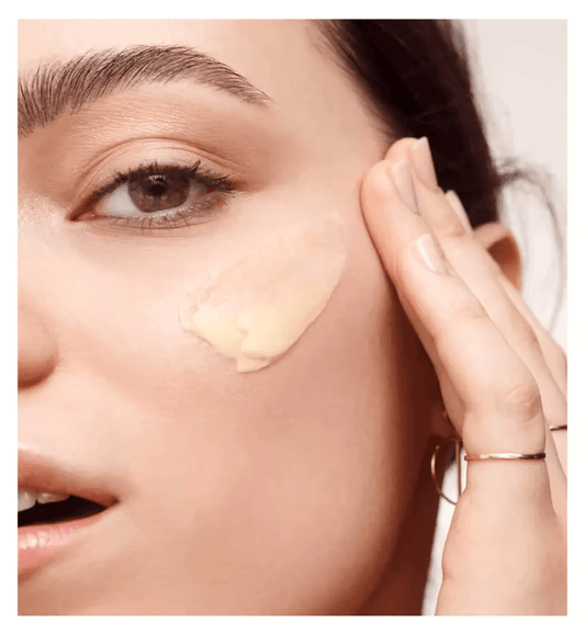 Woman applying Bobbi Brown Vitamin Enriched Face Base on her cheek for hydration and smooth makeup application.