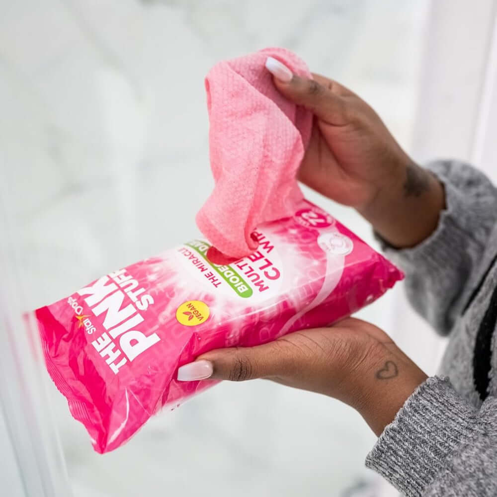 Person holding The Pink Stuff biodegradable multi-purpose cleaning wipes in a bathroom.