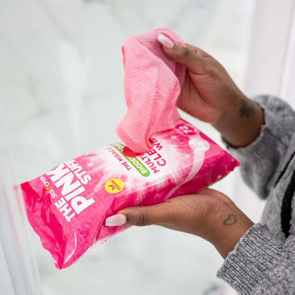 Person holding The Pink Stuff biodegradable multi-purpose cleaning wipes in a bathroom.