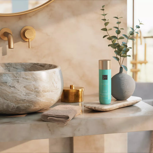 Bathroom counter with marble sink, gold faucet, and decorative items including a green bottle and gray vase.