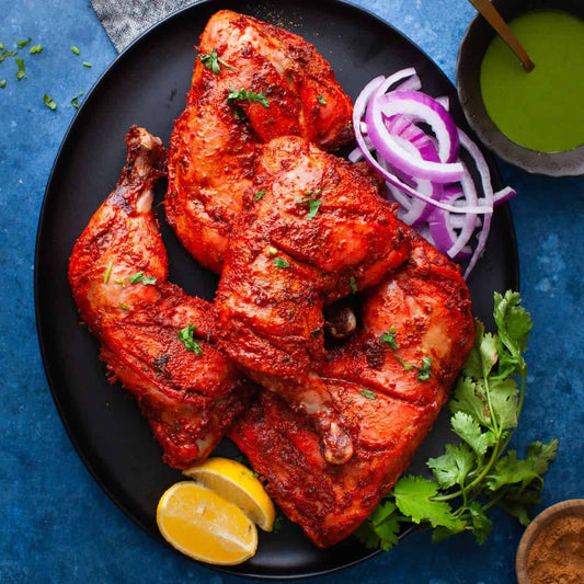 Plate of tandoori chicken with onion slices, lemon, and green sauce, showcasing vibrant red spices.