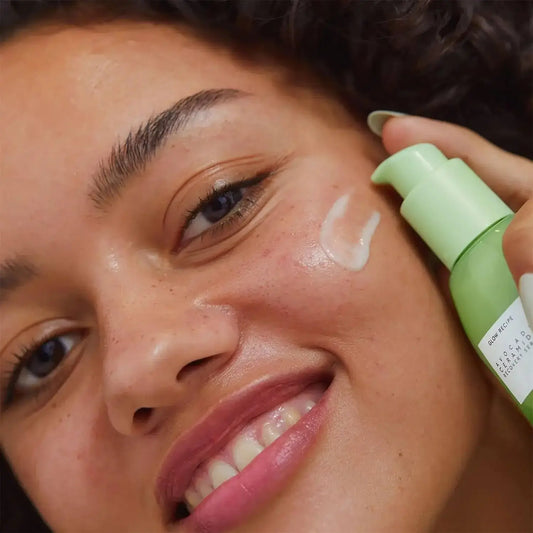 Happy woman applying GLOW RECIPE Avocado Serum on her face, showcasing its nourishing properties for healthy skin.