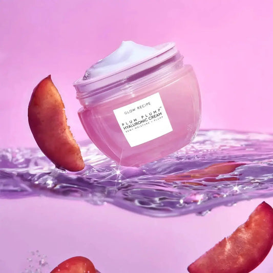 Glow Recipe Plum Plump Hyaluronic Cream in a refillable jar, surrounded by fresh plum slices, against a pink background.