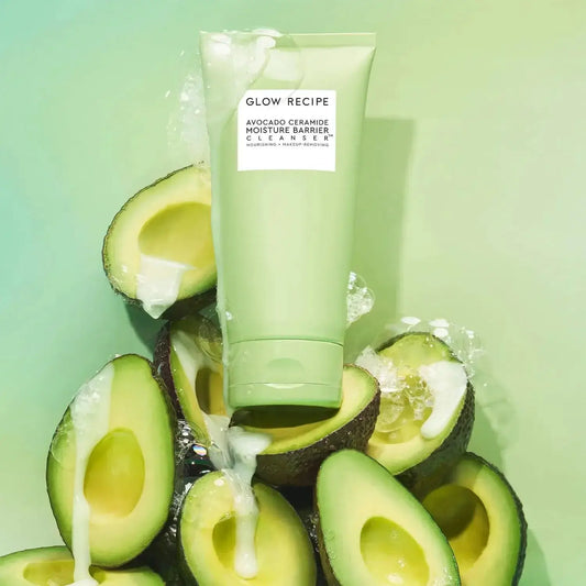 Glow Recipe Avocado Cleanser tube surrounded by fresh avocado halves on a vibrant green background.