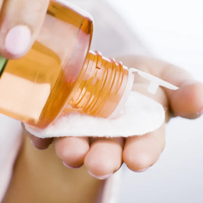 Woman pouring Pixi + Hello Kitty Glow Tonic onto a cotton pad for skincare application.