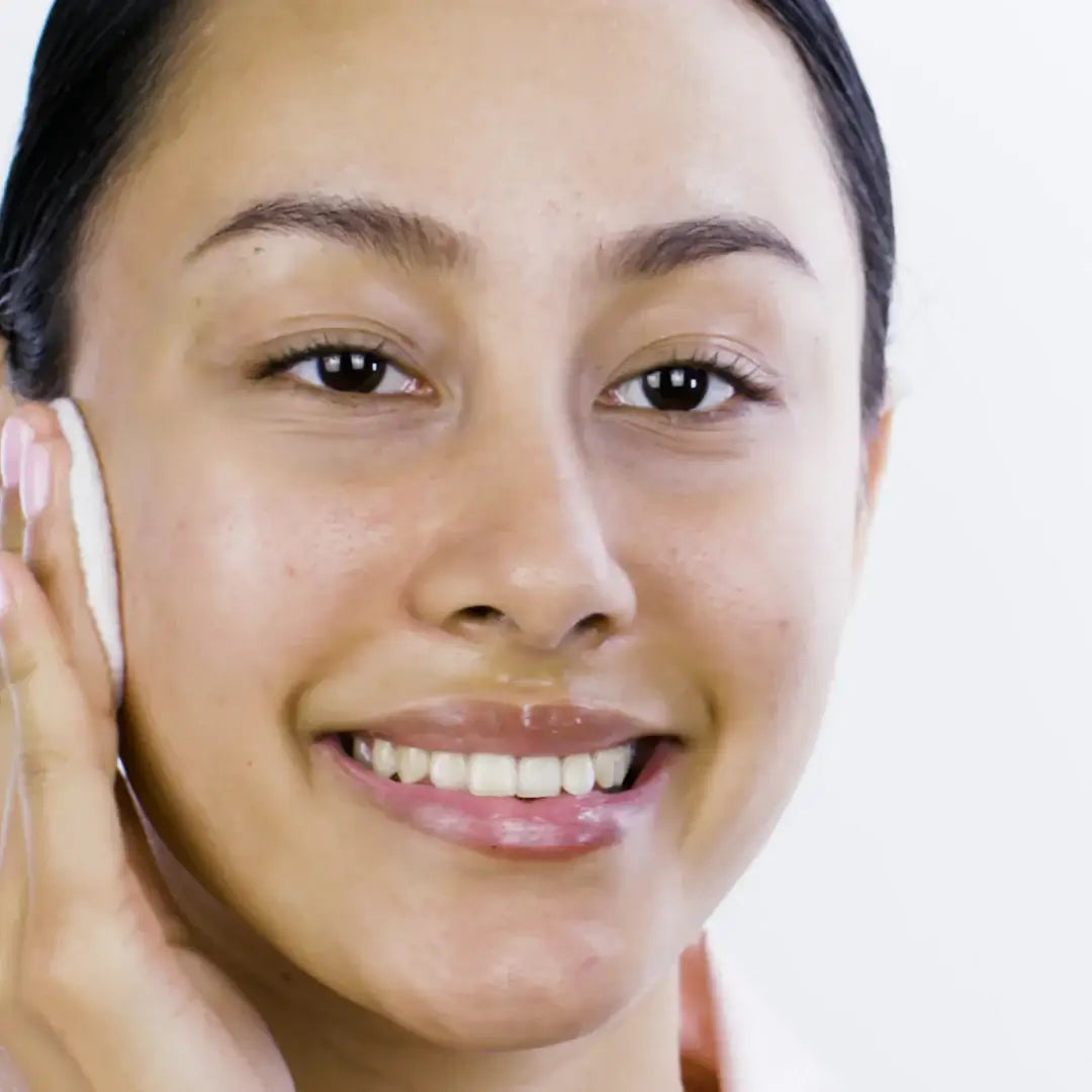 Woman applying Pixi + Hello Kitty Glow Tonic on her face using a cotton pad, showcasing radiant skin.