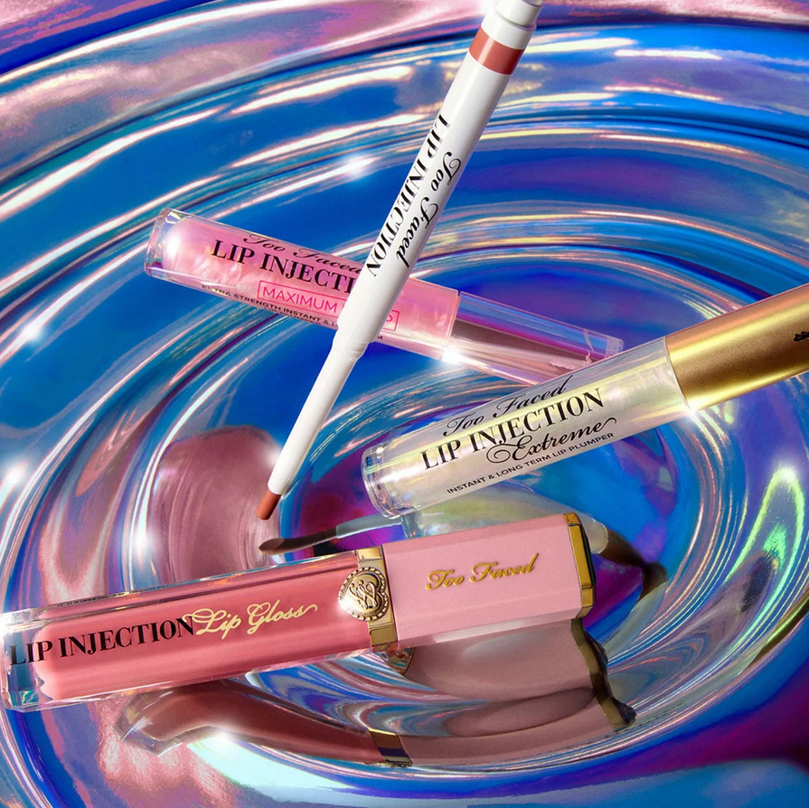 Too faced Lip gloss products with applicators on a reflective blue surface