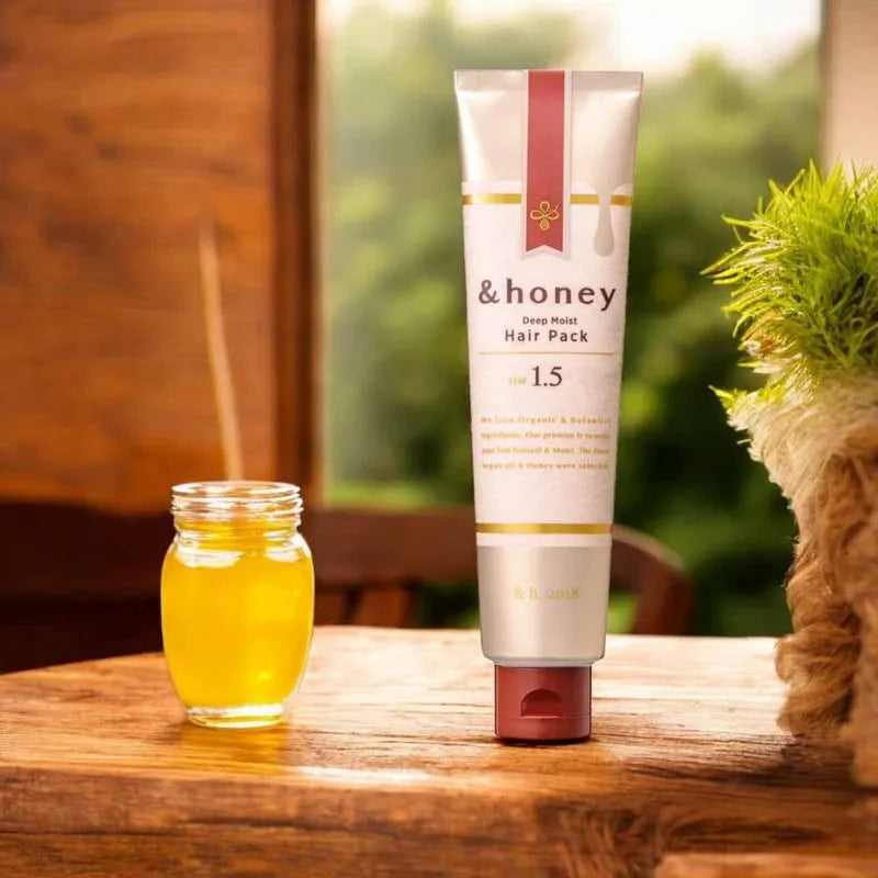 Tube of '& honey' hair pack and jar of yellow liquid on a wooden surface with a blurred natural background