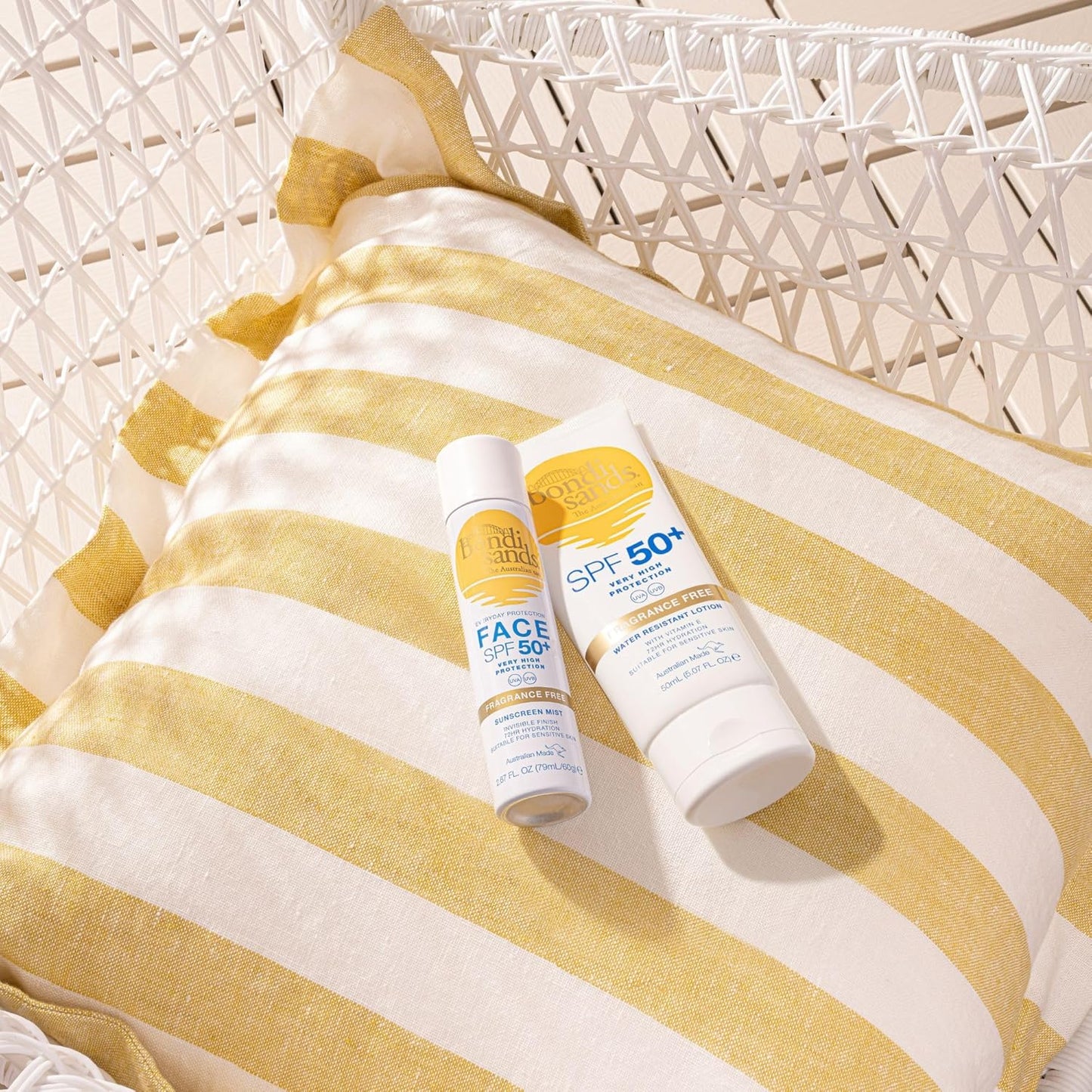 Two sunscreen bottles on a yellow and white striped towel with a wicker chair in the background.