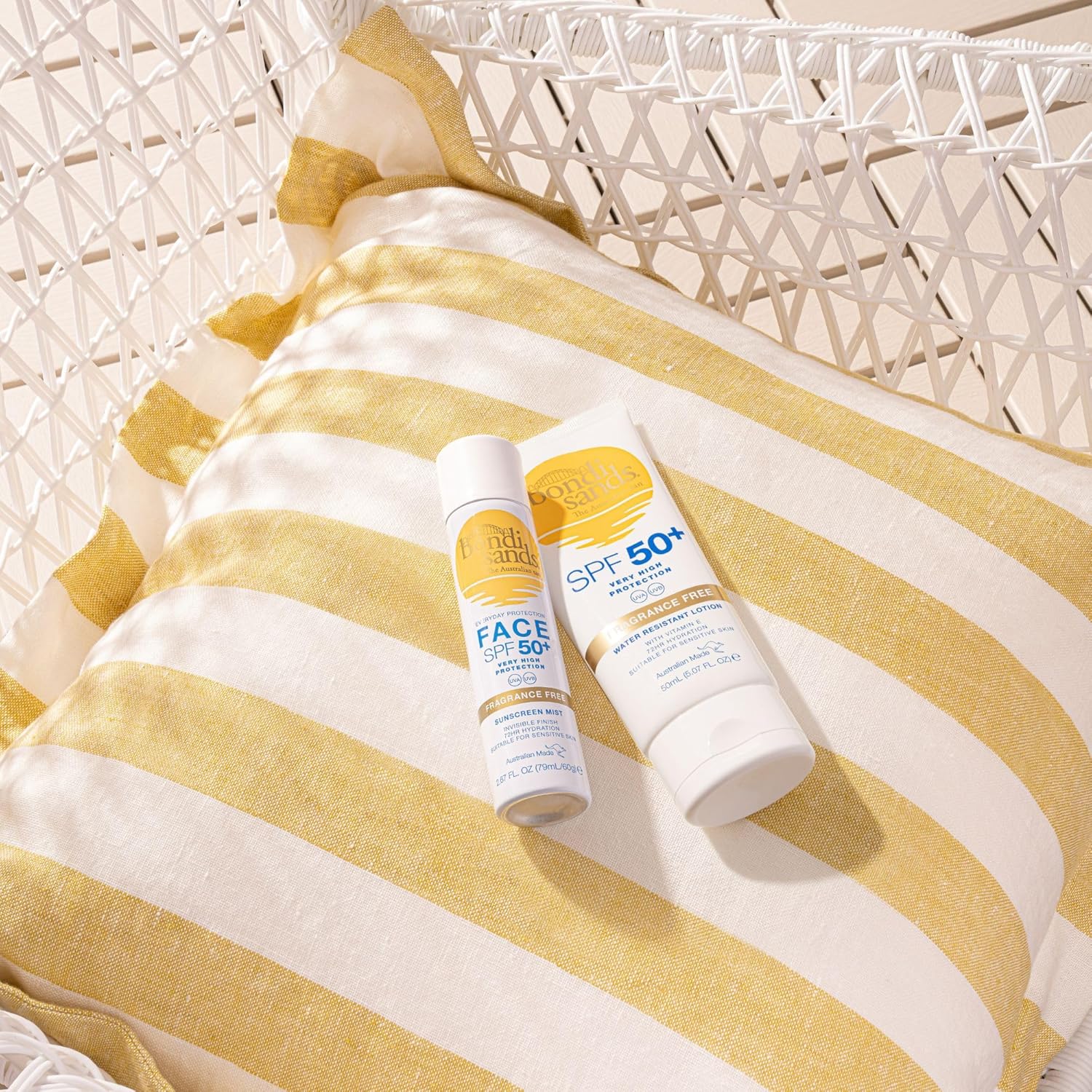 Two sunscreen bottles on a yellow and white striped towel with a wicker chair in the background.