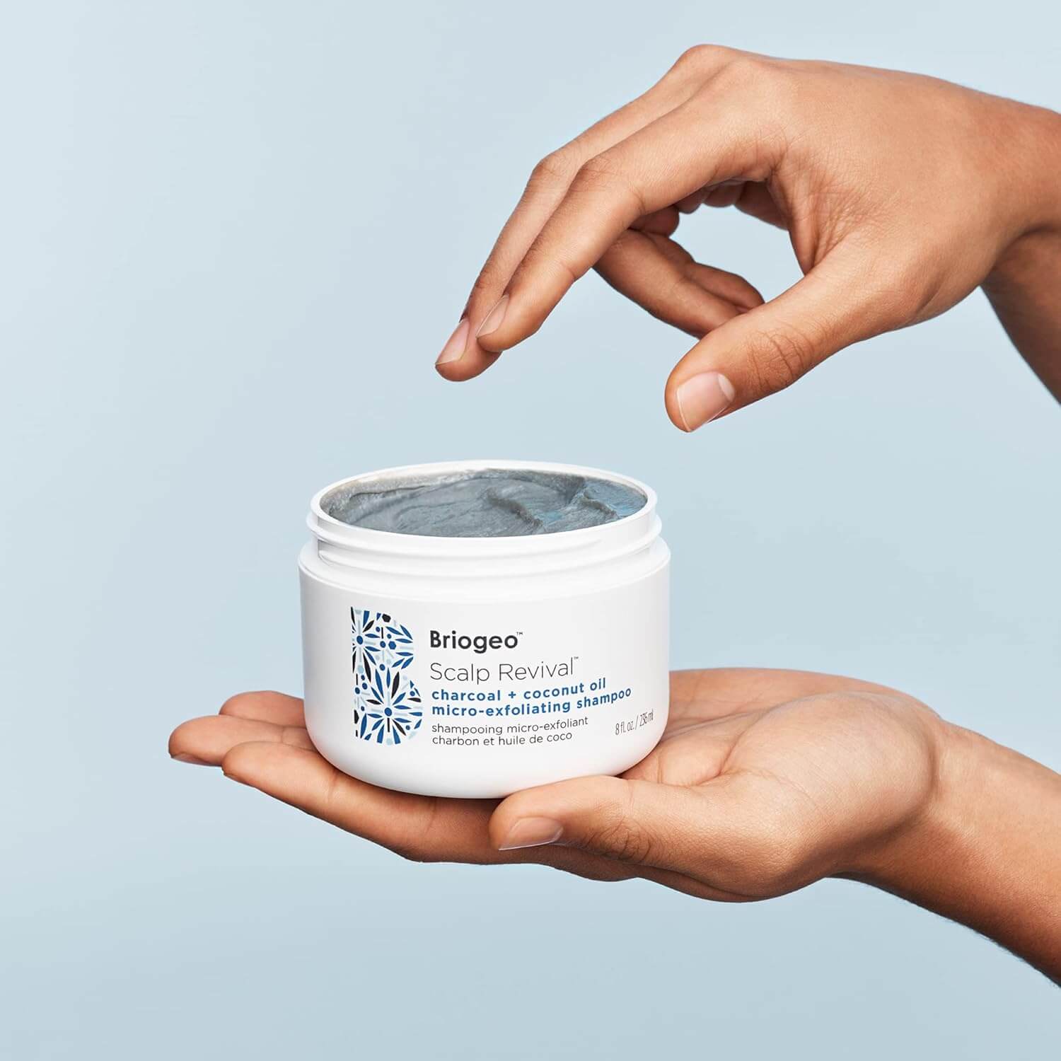 Hand holding a jar of Briogeo Scalp Revival product against a light blue background