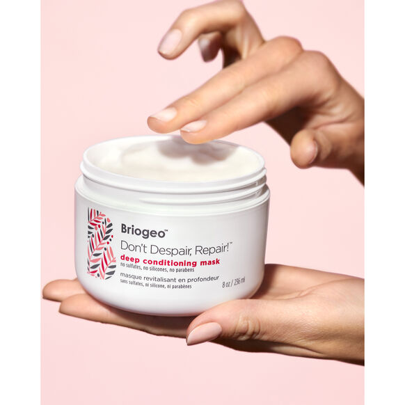 Hand holding a jar of Briogeo deep conditioning mask against a pink background