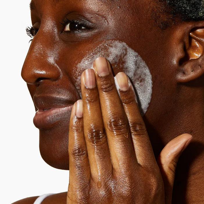 Person applying a facial CeraVe SA Smoothing Cleanser to their face with a neutral background