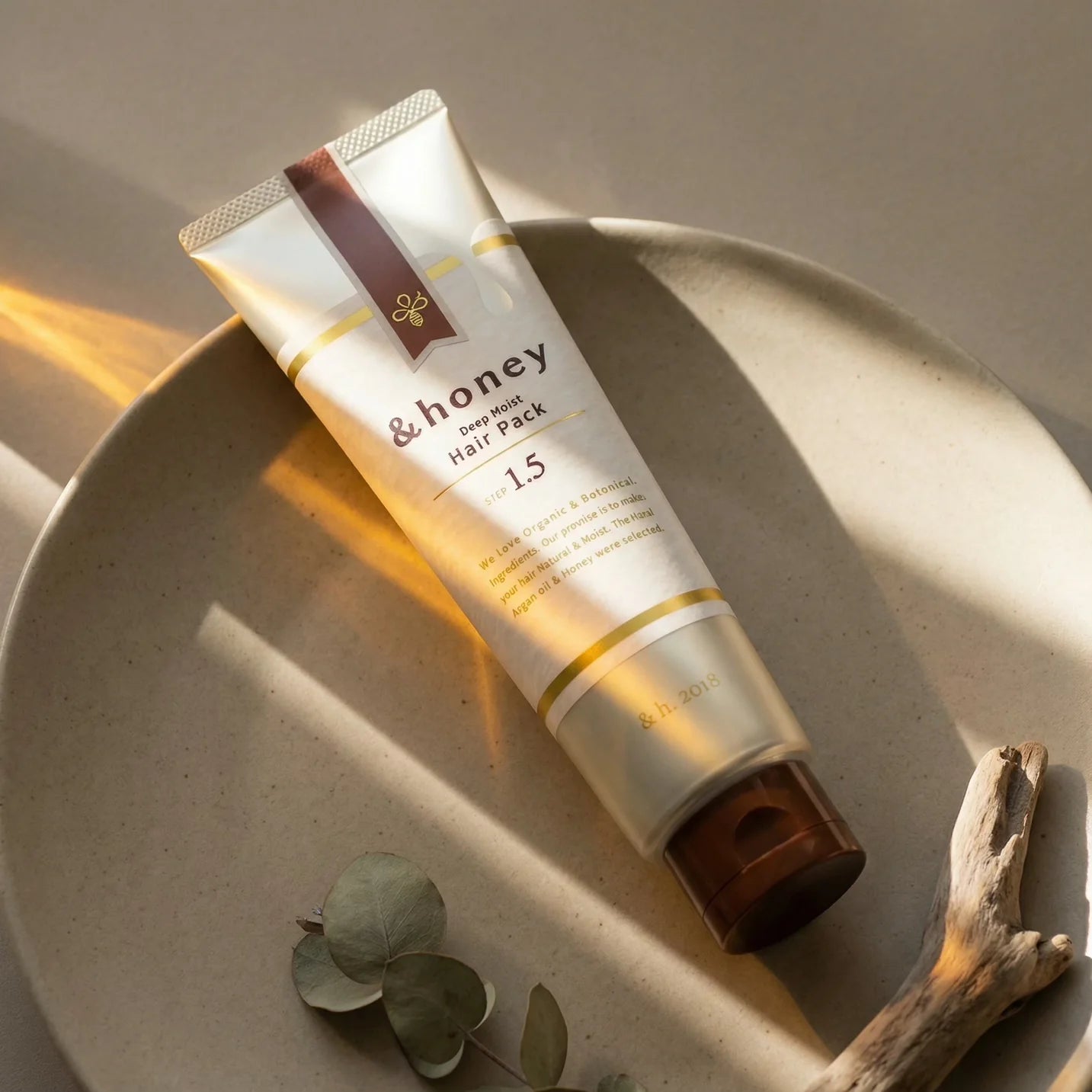 Tube of honey hair pack on a textured surface with natural elements